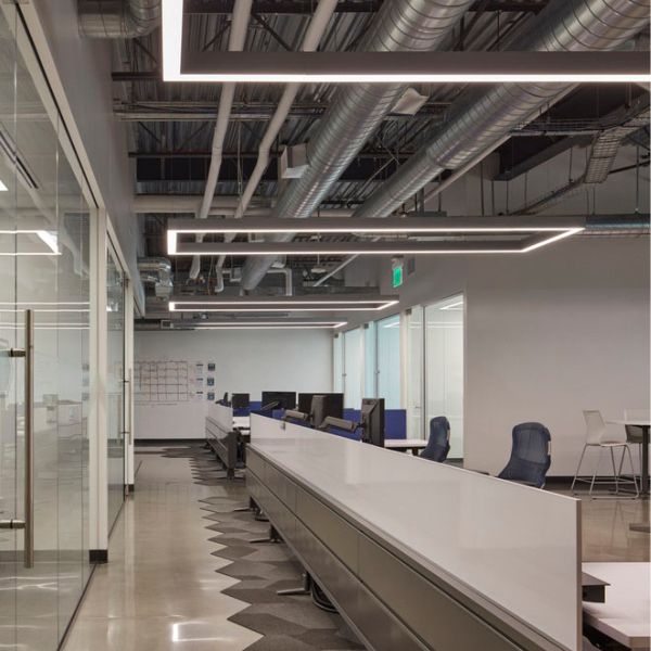 multiple interconnected matte grey closed-loop rectangular linear pendant lights suspended in a dynamic pattern above a long shared wooden work table in a modern open-plan office, providing even lighting for multiple workstations and collaborative groups.