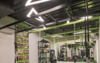 Architectural triangle-shaped linear light fixtures suspended in a luxury fitness center reception area, creating a dynamic geometric focal point for club members.