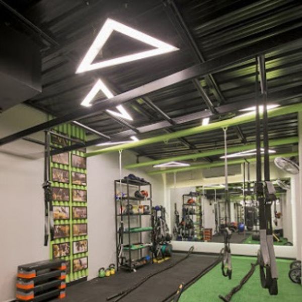 Architectural triangle-shaped linear light fixtures suspended in a luxury fitness center reception area, creating a dynamic geometric focal point for club members.